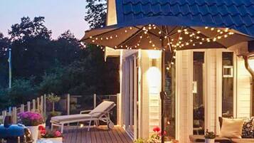 Una terraza con una silla de descanso, mobiliario exterior e iluminación con luces colgantes.