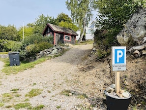 A gravel path leading to a rustic wooden building with a red roof, a parking sign, and a stone wall.