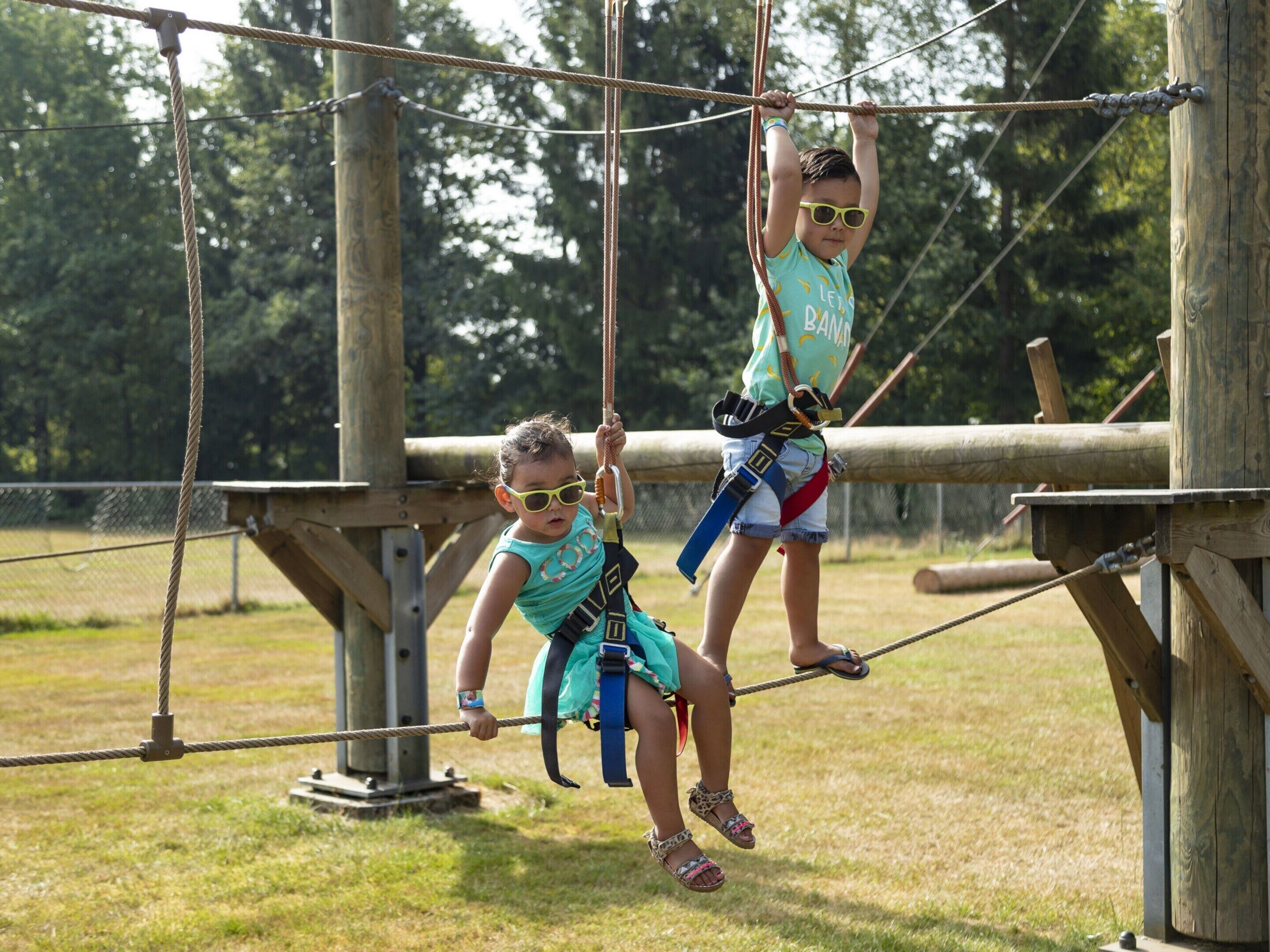 Two children on a rope bridge at an outdoor adventure park.