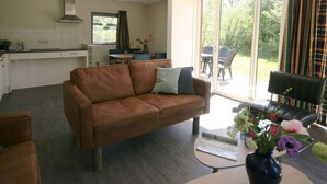 A modern living room with a brown sofa, a coffee table with a vase of flowers, and a view of the garden through large sliding glass doors.