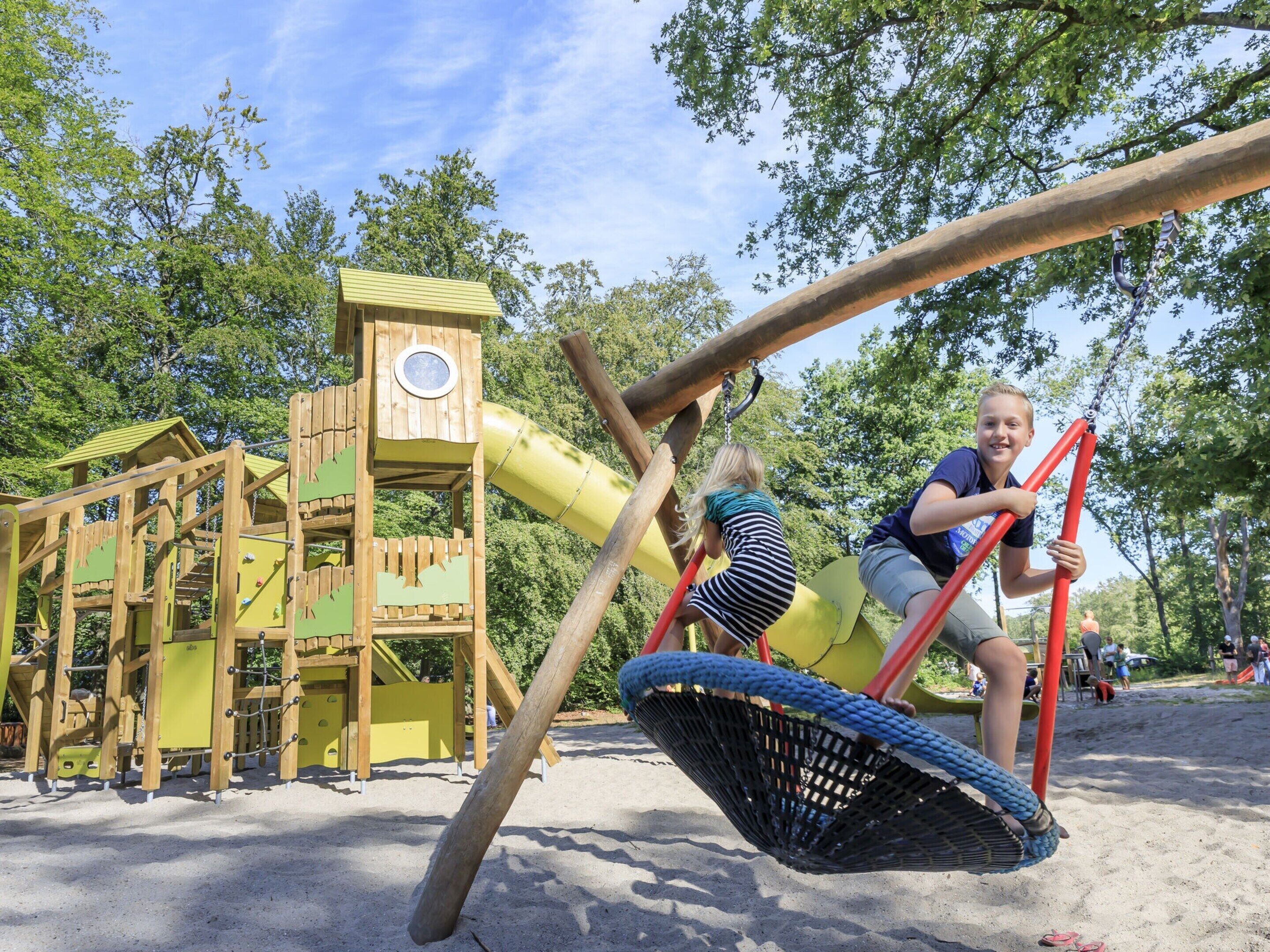 A playground with a wooden climbing structure and a yellow slide.