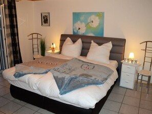 A neatly made bed with a blue and white blanket, a bedside table with a lamp, and a painting on the wall.