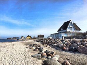 A coastal building with a thatched roof, surrounded by a rocky shoreline.