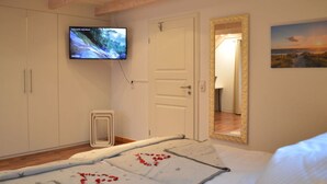 Ein Schlafzimmer mit einem Bett, einem an der Wand montierten Fernseher, einem Spiegel und einer Tür zu einem weiteren Raum.