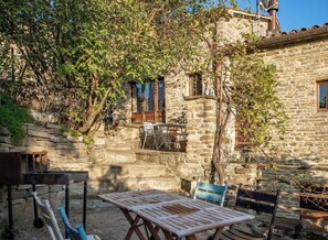 Un bâtiment en pierre doté d’un patio comprenant une table et des chaises en bois.