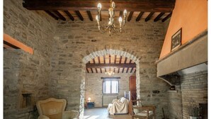 Une pièce rustique aux murs de pierre, avec un plafond en bois, un lustre, une cheminée et une fenêtre.