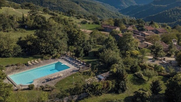 Une piscine entourée d’une végétation luxuriante et un village aux bâtiments d’architecture traditionnelle.