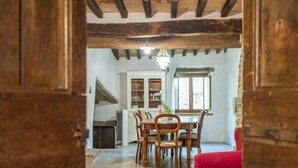 Un coin repas avec une table et des chaises en bois, un canapé rouge et une vue sur une cuisine équipée de placards et dotée d’une fenêtre.