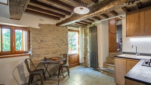Une cuisine rustique aux murs de pierre, avec des poutres en bois et un petit coin repas comprenant une table et des chaises.