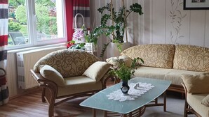Un salon comprenant un canapé, deux fauteuils, une table basse en verre et une fenêtre avec des rideaux.