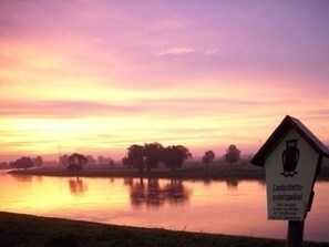 A sign with text in a foreign language, a body of water, and trees in the background. - A. Heyne Modern Retreat (Weinboehla)