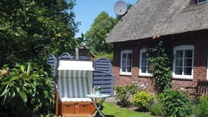 Une maison à toit de chaume, avec une antenne parabolique, une chaise à rayures et une petite table dans la cour.