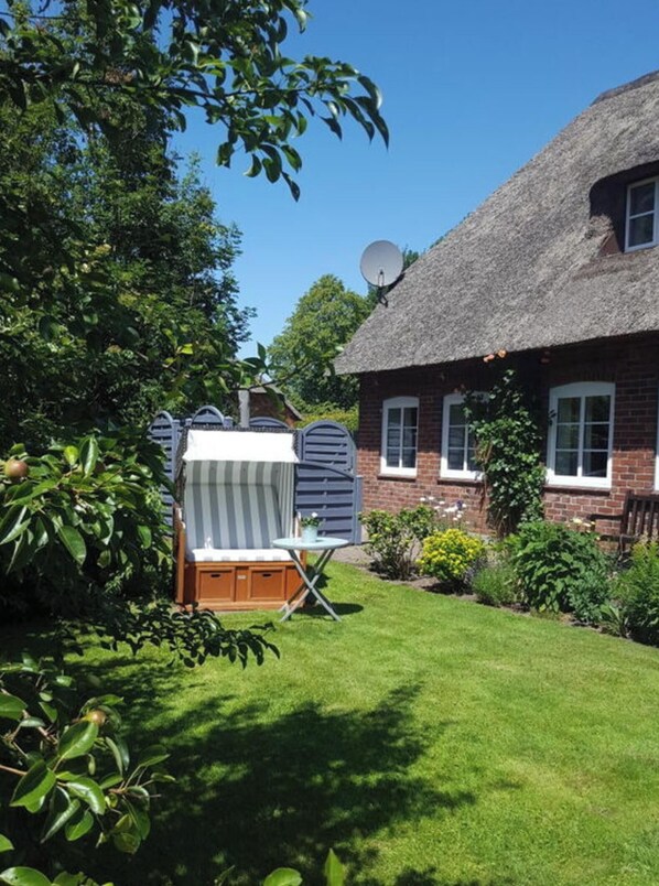 A thatched-roof house with a satellite dish, a striped chair, and a small table in the yard. - Holiday Apartment Wanlik Hus (Risum-Lindholm)