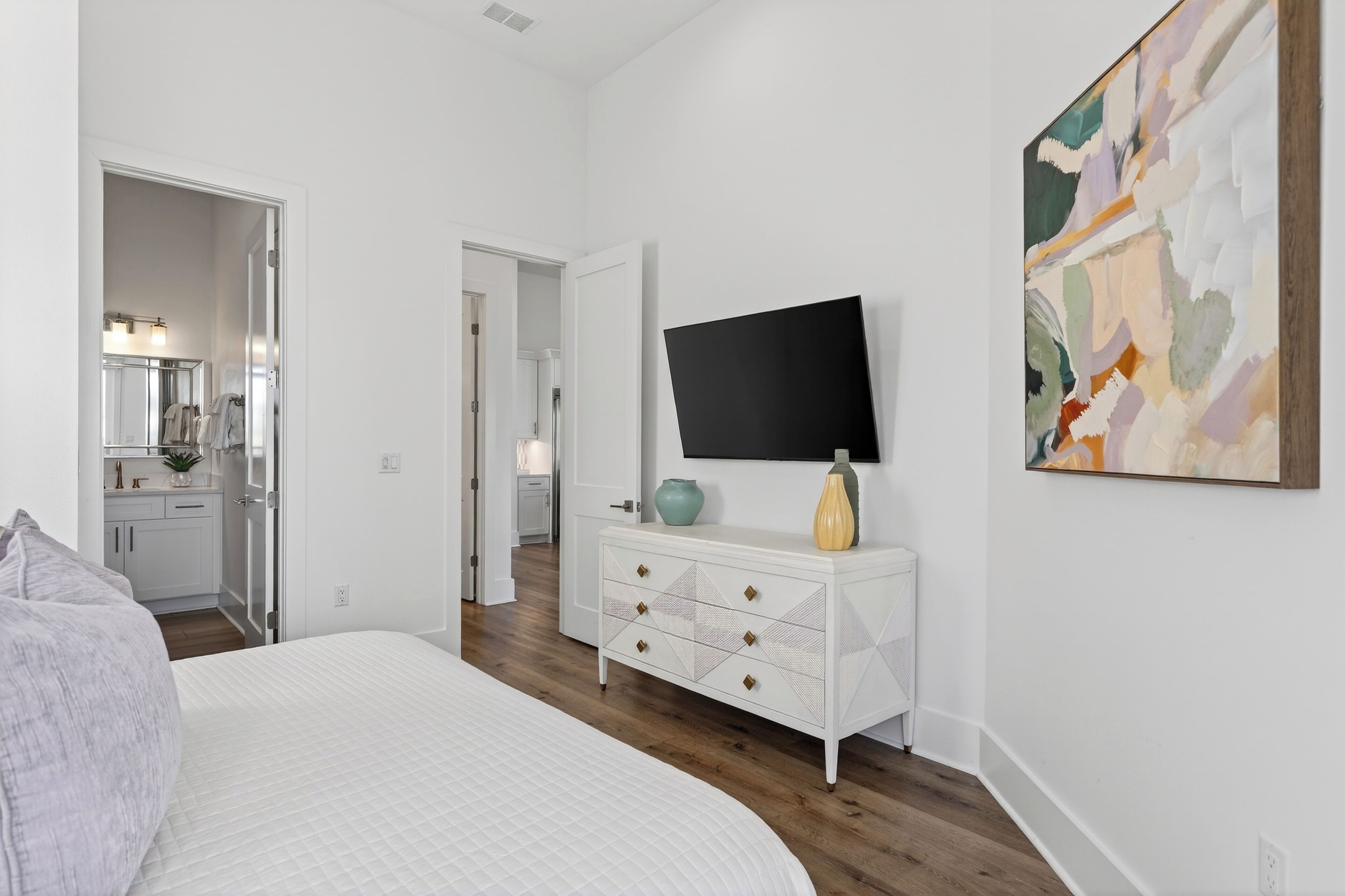 A bedroom with a bed, a dresser, a TV, and a painting.
