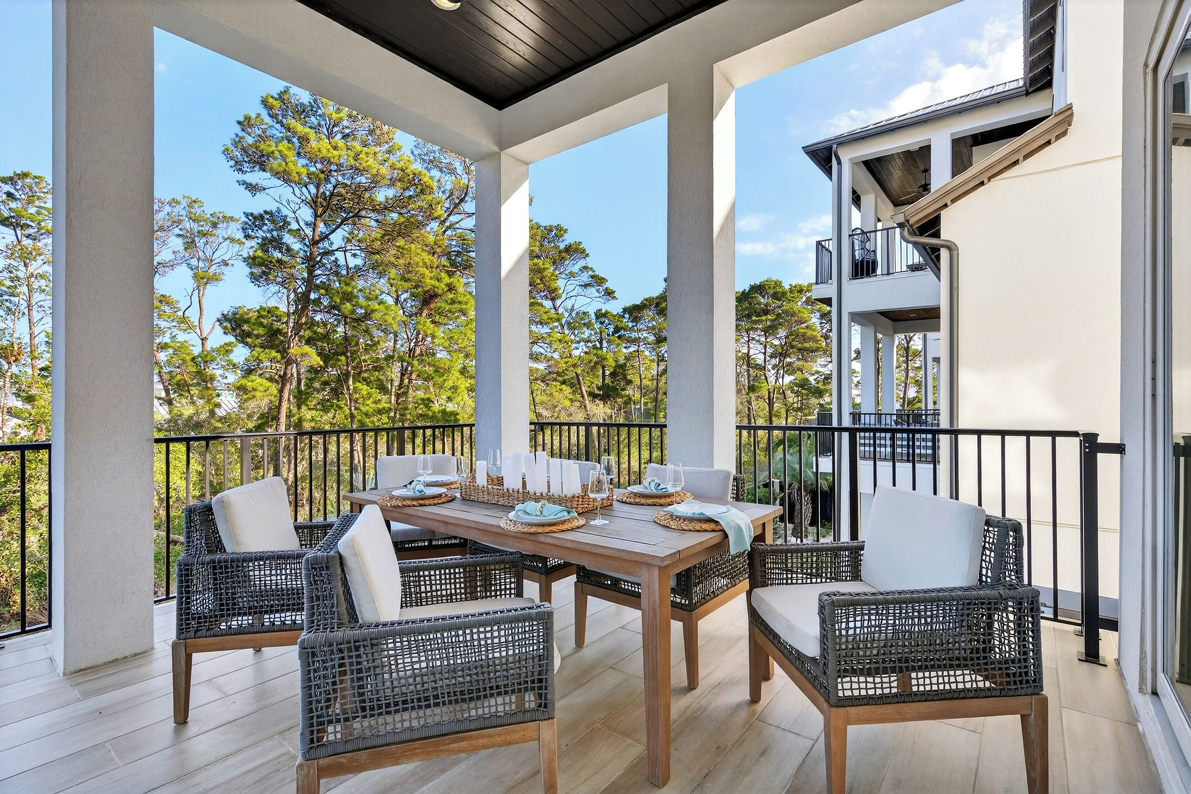 Un patio techado al aire libre con mobiliario de mimbre y una mesa de comedor lista para cuatro personas.