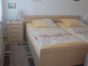 A bedroom with two beds, a bedside table, a lamp, and a clock. - Holiday Home Hermann (Butjadingen)