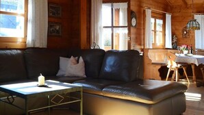 Un interior de madera acogedor con un sofá de cuero, una mesita con una vela y un comedor con una mesa dispuesta para dos.