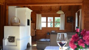Un interior rústico de madera con un horno de piedra, una mesa de comedor con una copa de vino y una cesta sobre el horno.