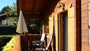 Una terraza de madera con dos sillas, una mesa, una sombrilla y una puerta.