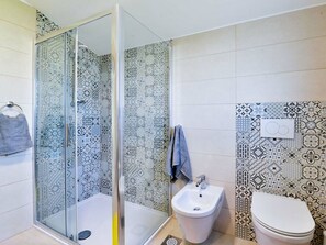 Un baño con baldosas estampadas, cabina de ducha de vidrio, un bidé y un inodoro.