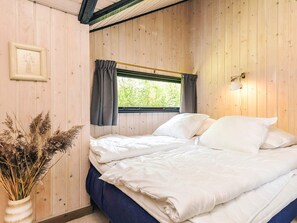 A wooden-paneled room with a bed, a window with curtains, and a wall-mounted lamp.