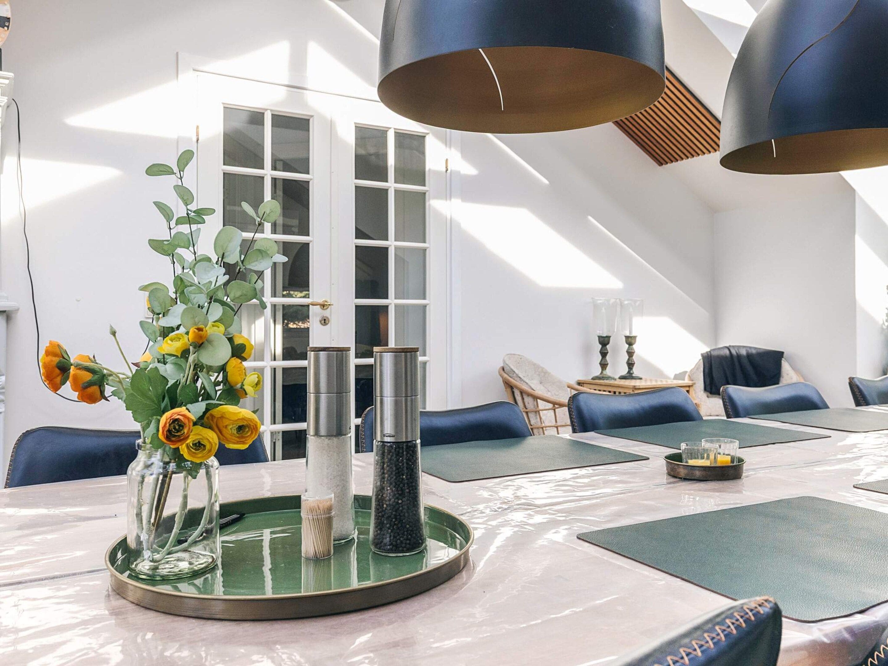 A modern dining area with a round table, blue chairs, and a vase of yellow flowers.