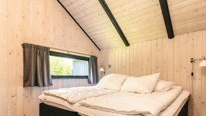Et soveværelse med en seng, et vindue med gardiner, en lampe og trævægge.