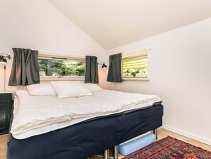 Ein Schlafzimmer mit einem Bett, zwei Vorhängen an den Fenstern, einem Nachttisch und einer Lampe.