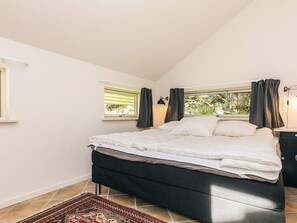 Un dormitorio con cama, dos ventanas, una mesita de noche y una alfombra.