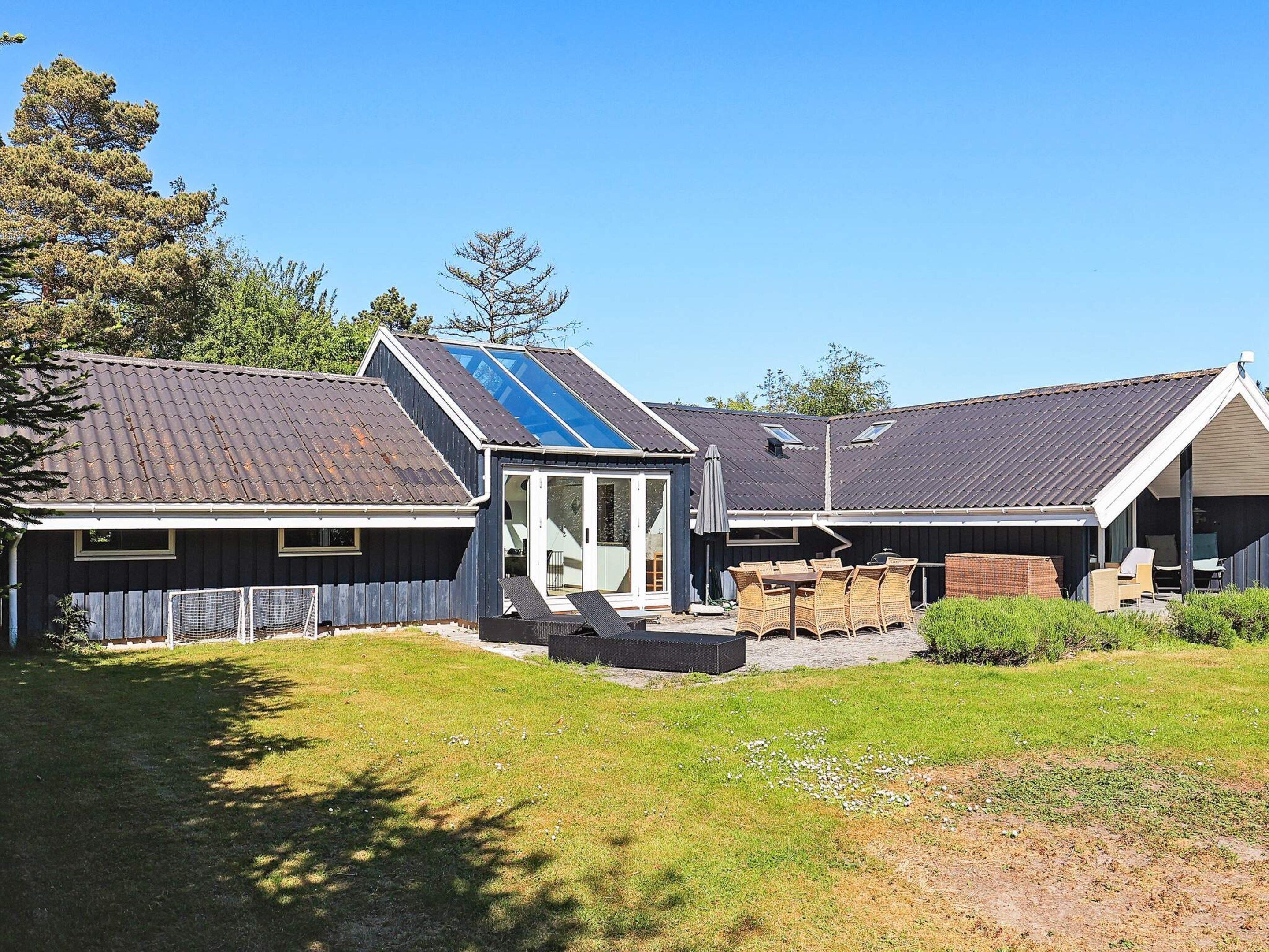 Une maison avec un toit en pente, un patio couvert avec des meubles d’extérieur et une cour clôturée.