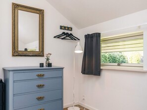 Una habitación con un aparador azul, un espejo con marco decorativo, un perchero, una lámpara de pie y una ventana con vistas a zonas verdes.