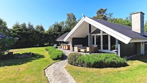Et moderne hus med en overdækket terrasse, en sti af natursten og frodig beplantning.