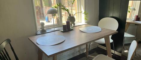 A dining area with a wooden table, two white chairs, a potted plant, and a window with blinds.