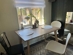 En matplats med ett träbord, två vita stolar, en krukväxt och ett fönster med persienner.
