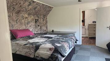 A bedroom with a floral-patterned headboard, a bed with a black and white floral bedspread, a pink pillow, and a bedside table with a lamp.