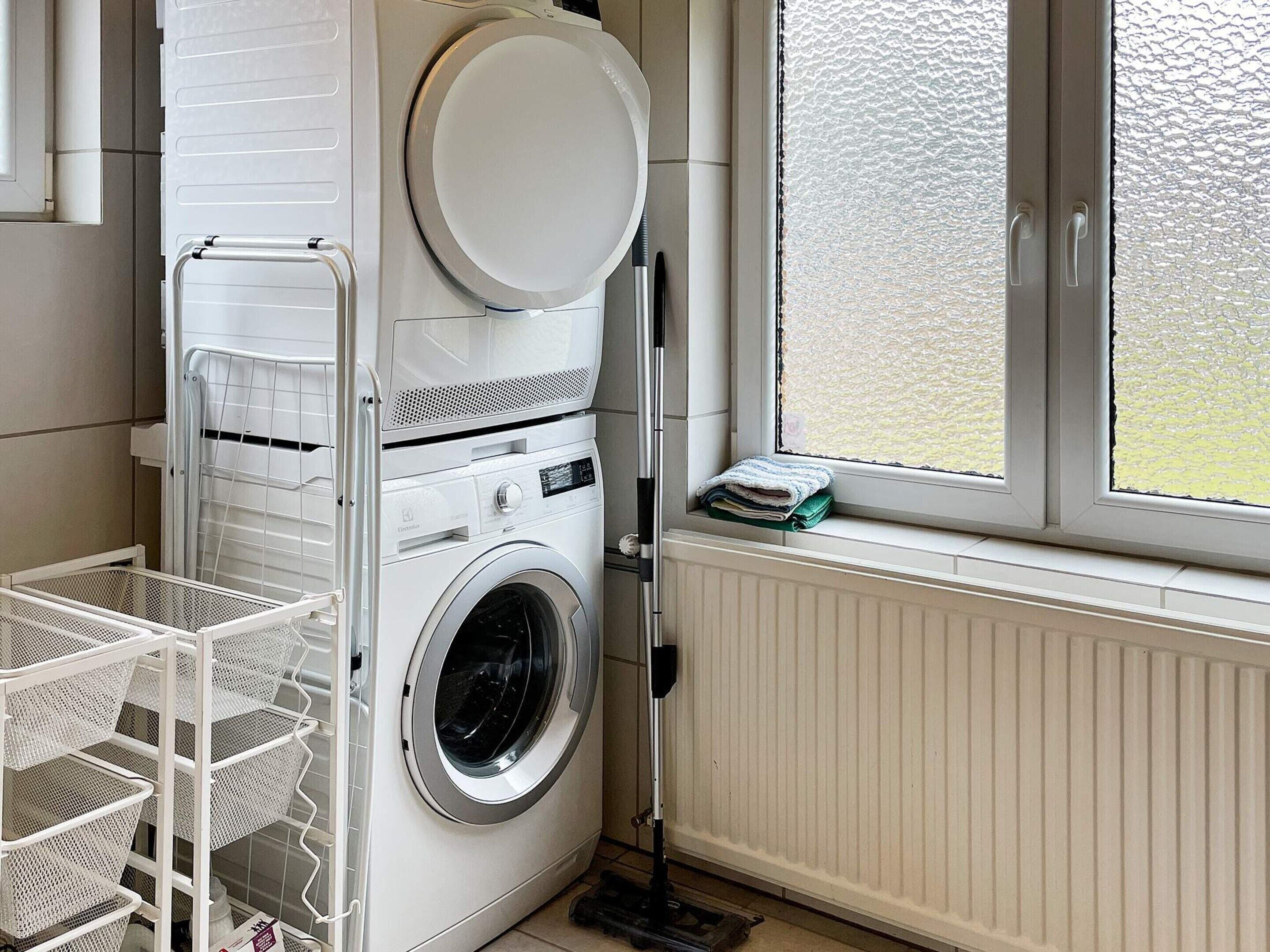 A laundry area with a washing machine, a drying rack, and a window with a view.