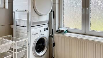 A laundry area with a washing machine, a drying rack, and a window with a view.