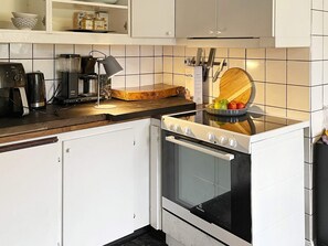 A kitchen with white cabinets, a black stove, and a wooden cutting board with fruits.