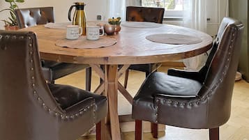A round wooden dining table with four upholstered chairs, a coffee pot, and decorative items on placemats.