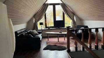A cozy attic room with a wooden floor, a black leather sofa, a small table, and a TV.