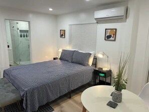 A bedroom with a bed, bedside tables, a desk, a chair, a potted plant, and an air conditioning unit. - "Stylish Studio Retreat - Outdoor Patio & kitchen (Miami)