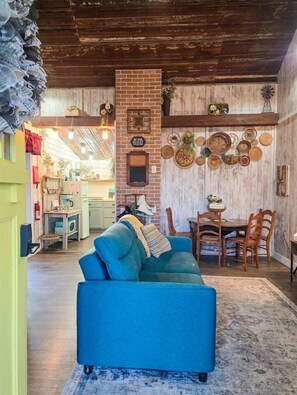 Ein gemütliches Wohnzimmer mit einem blauen Sofa, einem Kamin aus Ziegeln und einem Essbereich mit Holzsesseln.