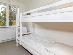 A bunk bed with a white frame and mattress, a window with a view of trees, and a radiator on the wall.