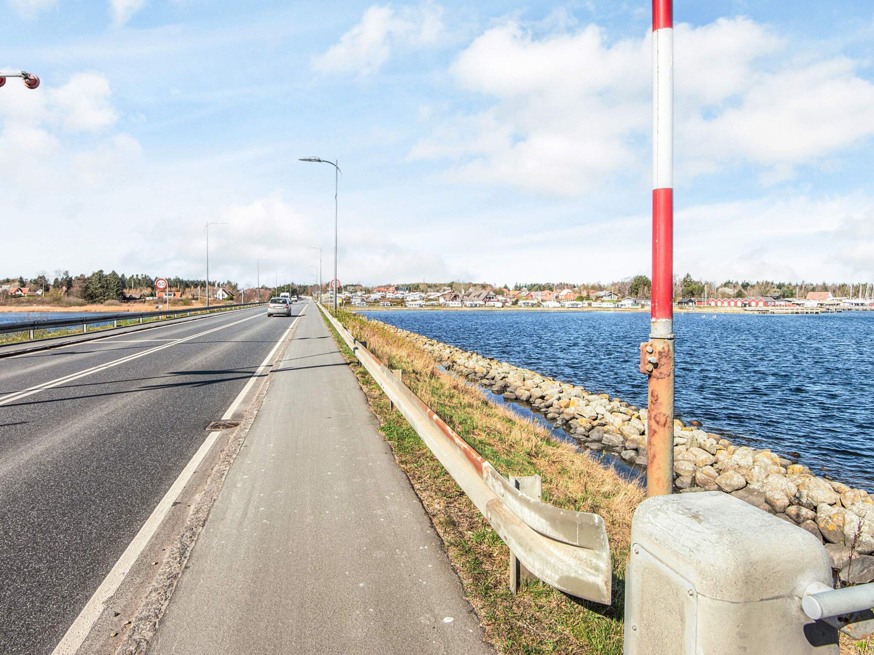Una carretera costera con una senda peatonal que bordea una masa de agua, con un cartel de límite de velocidad y un poste rojo y blanco.