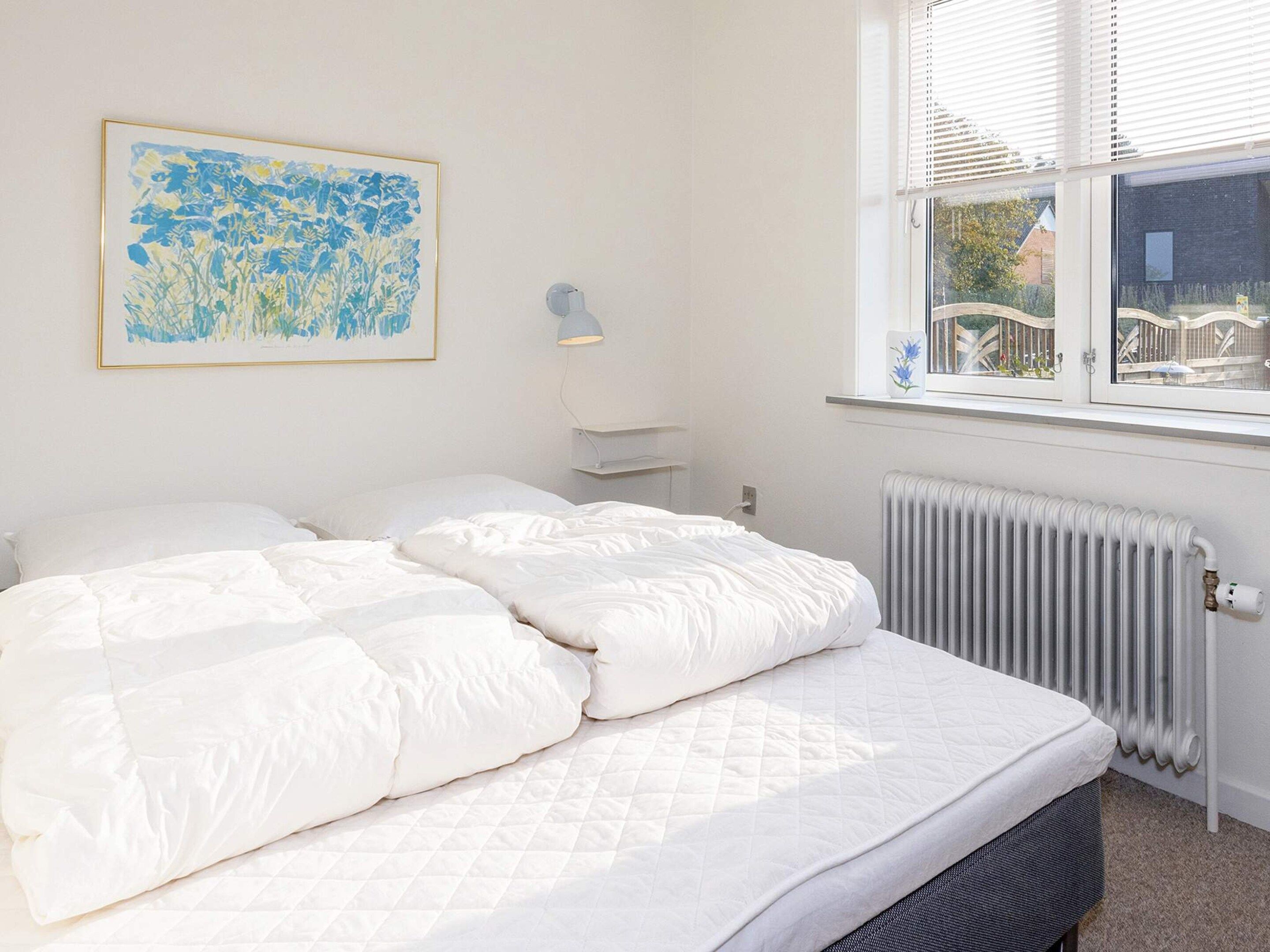Quarto com cama, radiador, janela com persianas e luminária na parede.