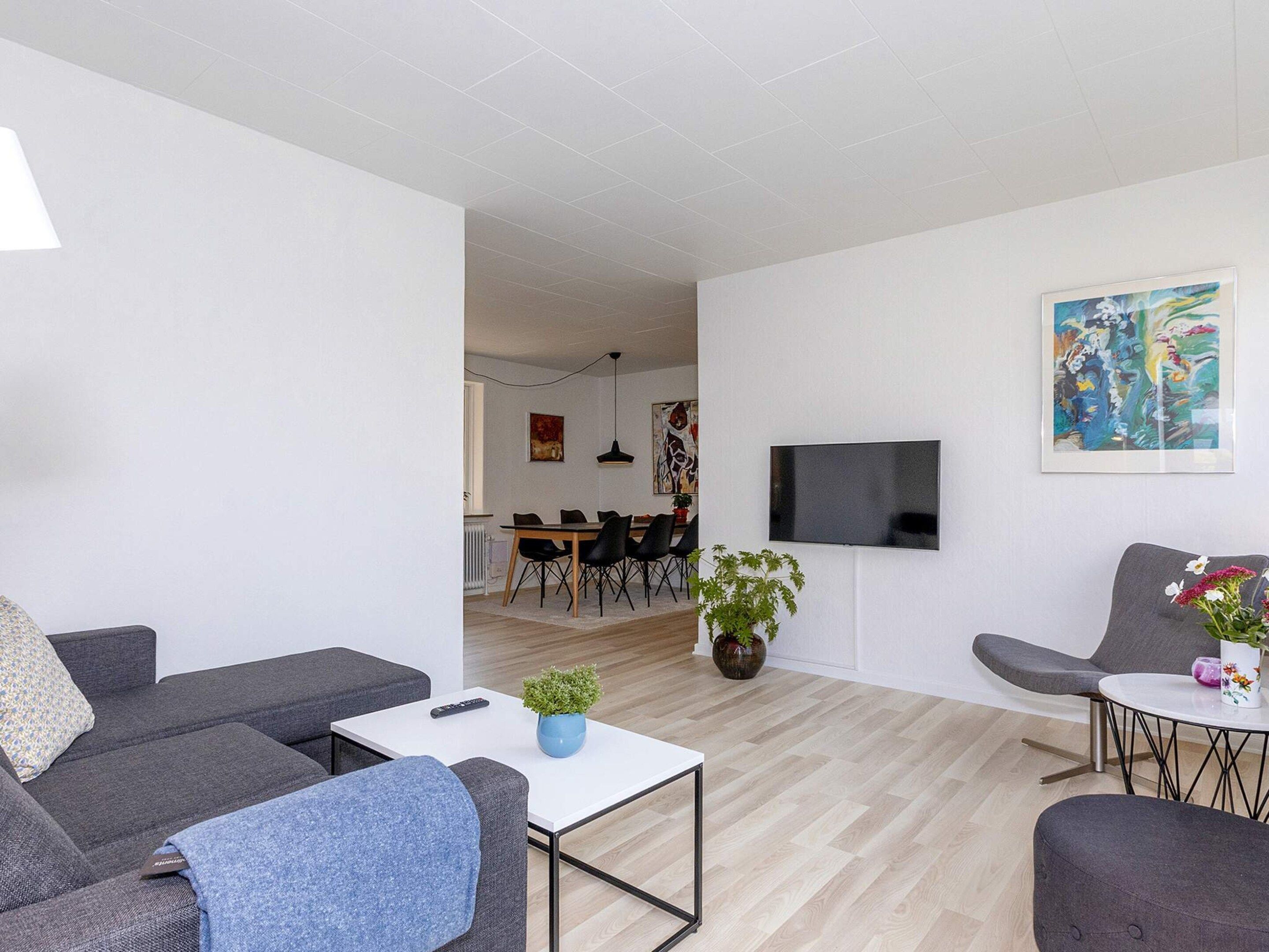 A modern living room with a sofa, armchair, coffee table, and a TV mounted on the wall.