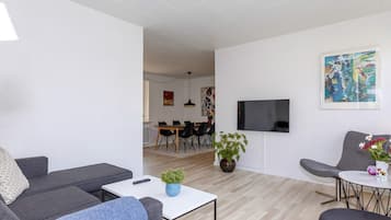 Uma sala de estar moderna com sofá, poltrona, mesa de centro e televisão na parede.