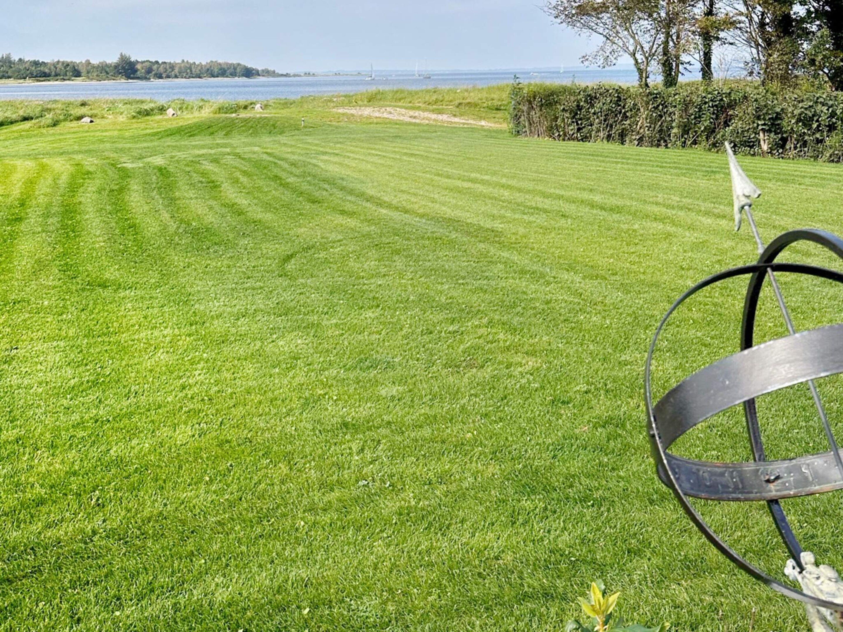 A well-maintained grassy area with a metal sculpture, a body of water, and a distant view of a bridge.