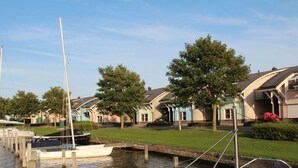A marina with boats docked, surrounded by houses with sloped roofs and a grassy area with trees. - Dijkvilla on the Ijsselmeer (Makkum)