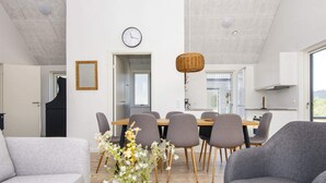 A modern living room with a sofa, a chair, a dining table with chairs, a vase with flowers, and a clock on the wall. - 5 Star Holiday Home in Romo (Rømø)